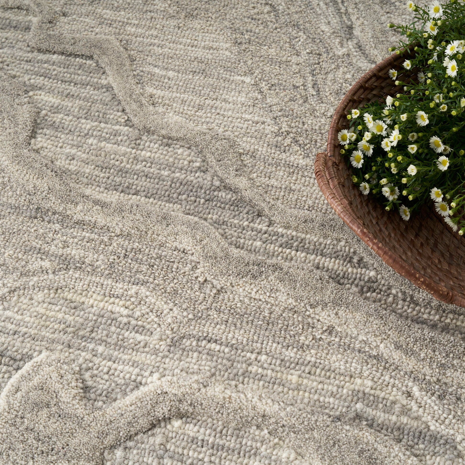 Beige textured rug with a wavy pattern; brown wicker basket of white daisies sits at the top-right.