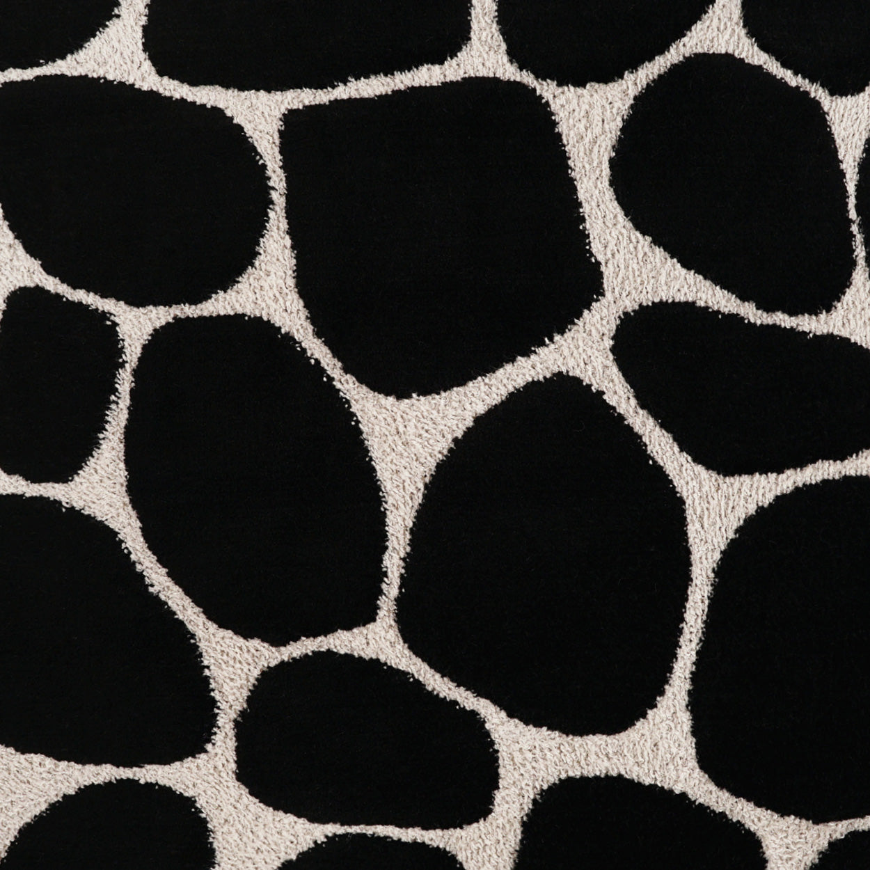 Beige rug featuring large black irregular pebble shapes for a bold stone-pattern look.