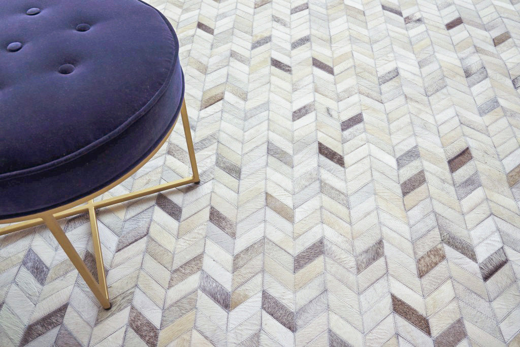 Purple round tufted ottoman with gold metal legs on a beige chevron rug.