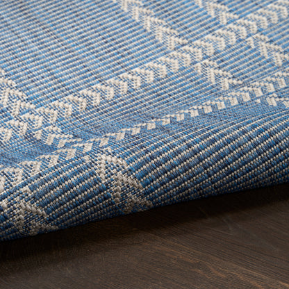Blue and white woven cotton rug with chevron geometric patterns, folded on a dark wood floor.