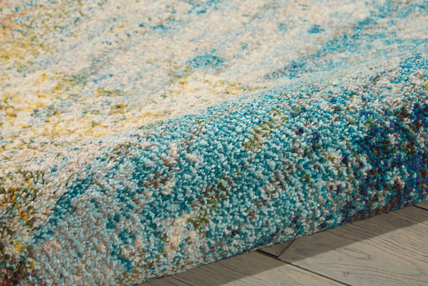 Close-up of a multicolor shag rug with blue, teal, and yellow tufted pile on a wooden floor.