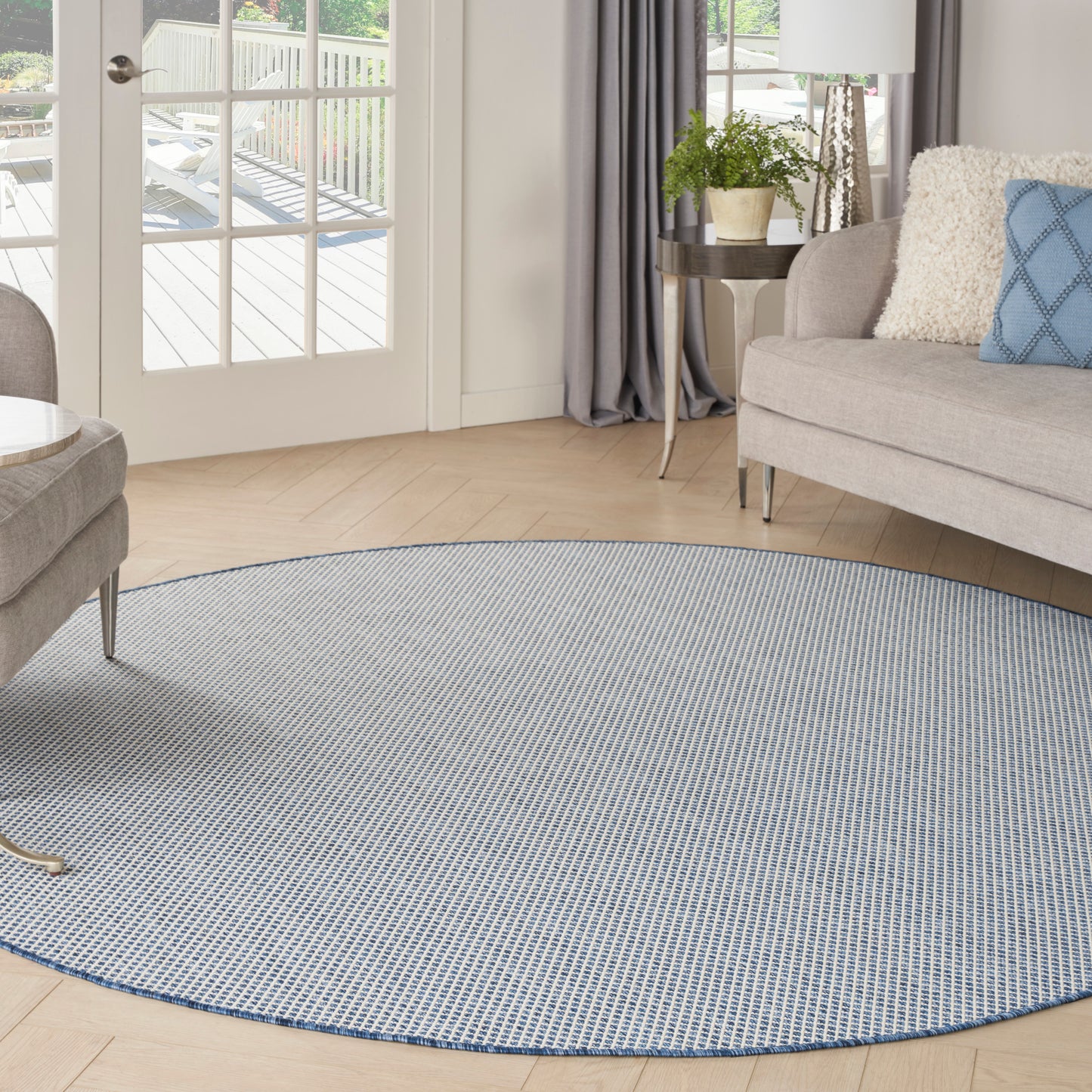 Round blue-gray woven area rug on light wood floor in a bright contemporary living room with a sofa and plants.