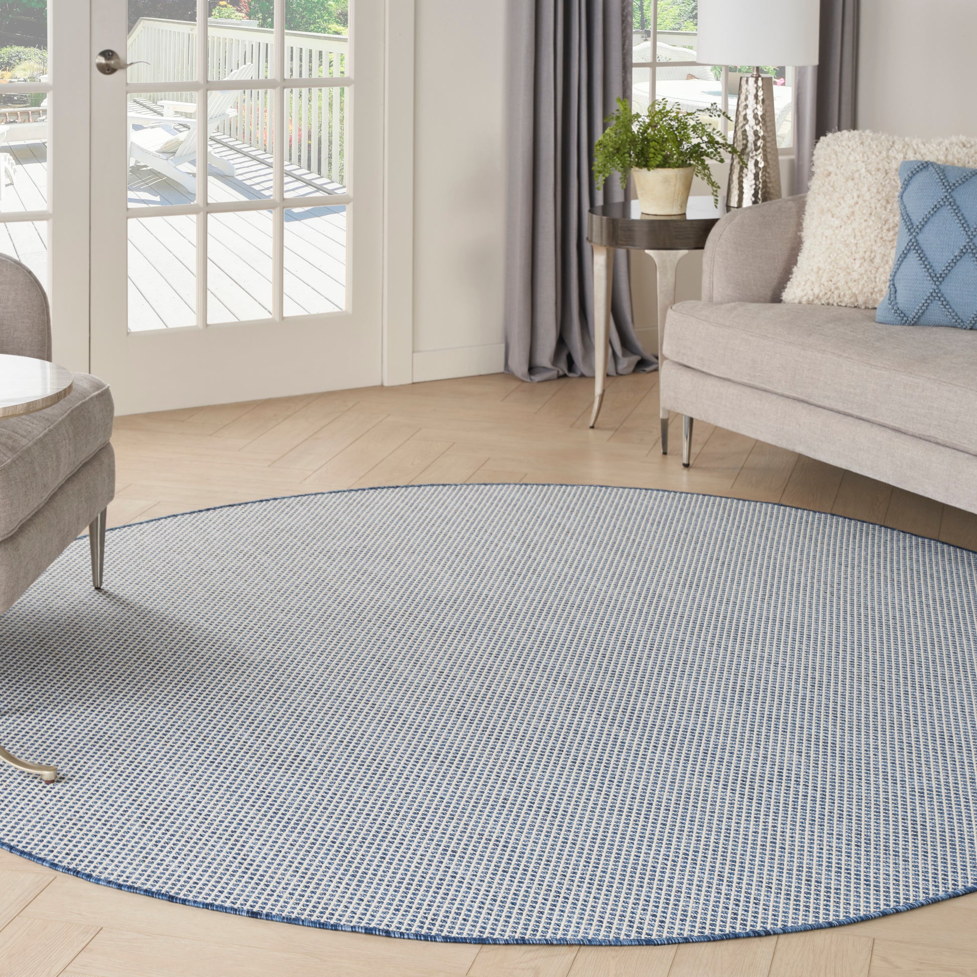 Round blue-gray woven area rug on light wood floor in a bright contemporary living room with a sofa and plants.