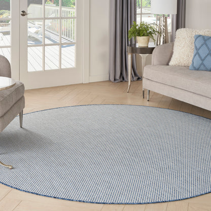 Round blue-gray woven area rug on light wood floor in a bright contemporary living room with a sofa and plants.