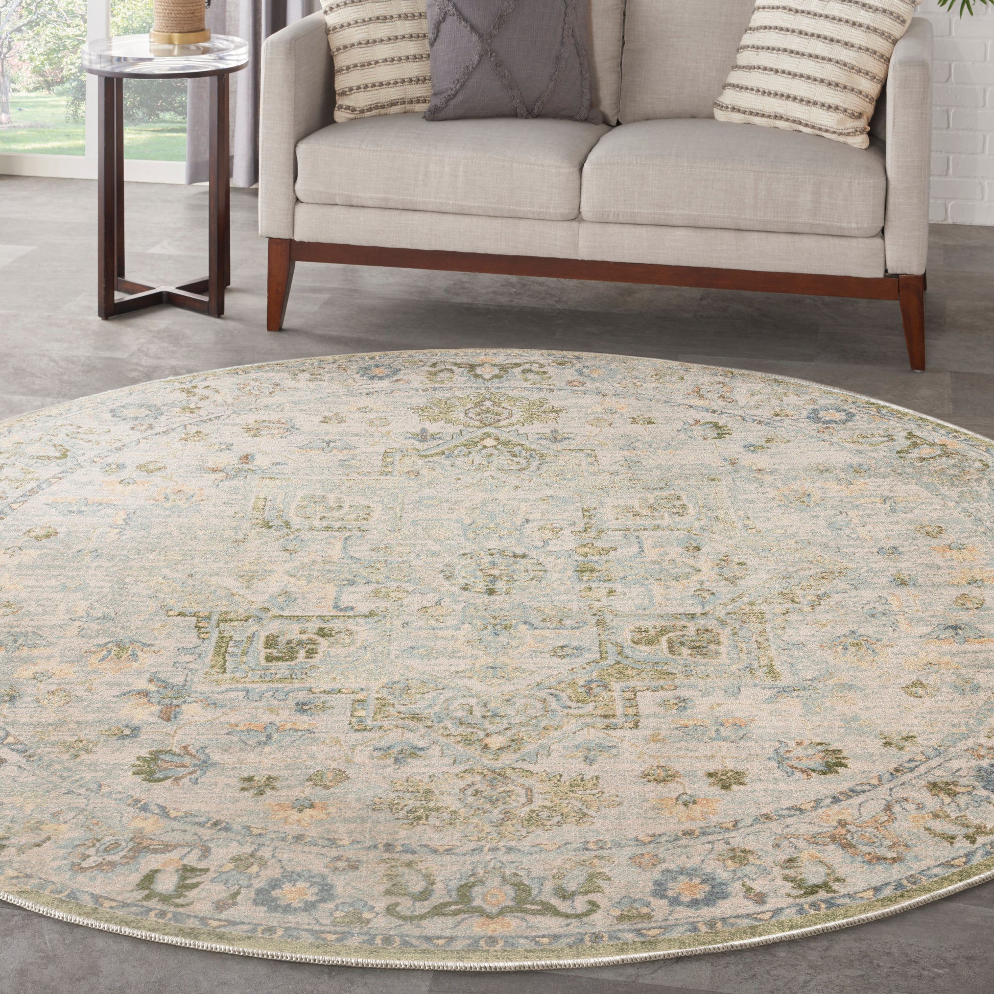 Round ivory rug with pale blue-green and yellow medallion motif under a beige sofa and wood side table.