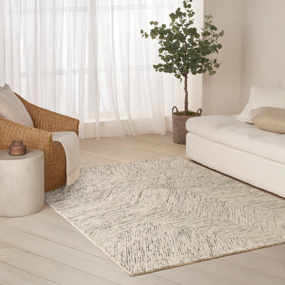 Neutral living room with a textured gray-beige area rug, white sofa, rattan chair, potted plant, and sheer curtains.