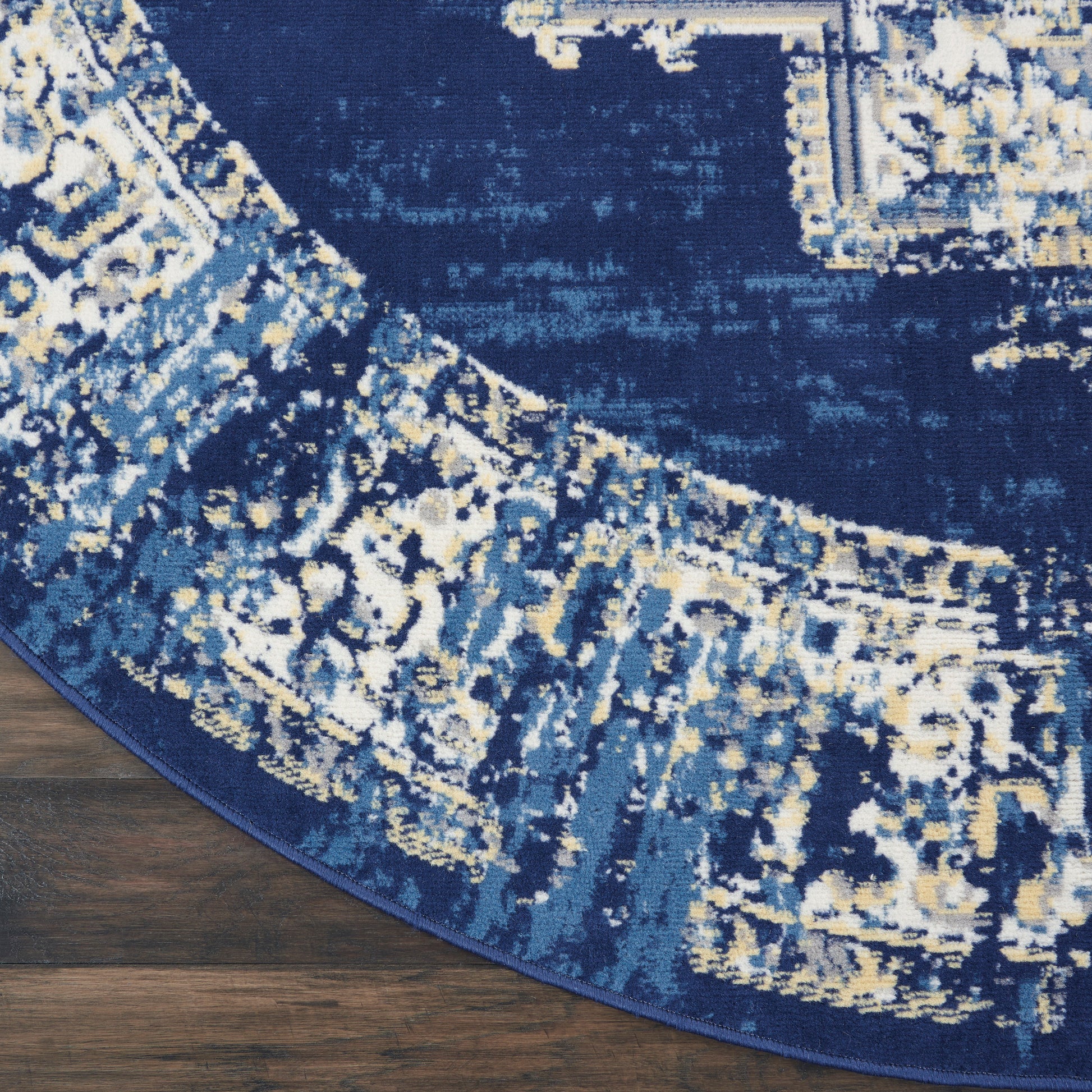 Round navy rug with abstract ivory and pale blue pattern on dark wood floor.
