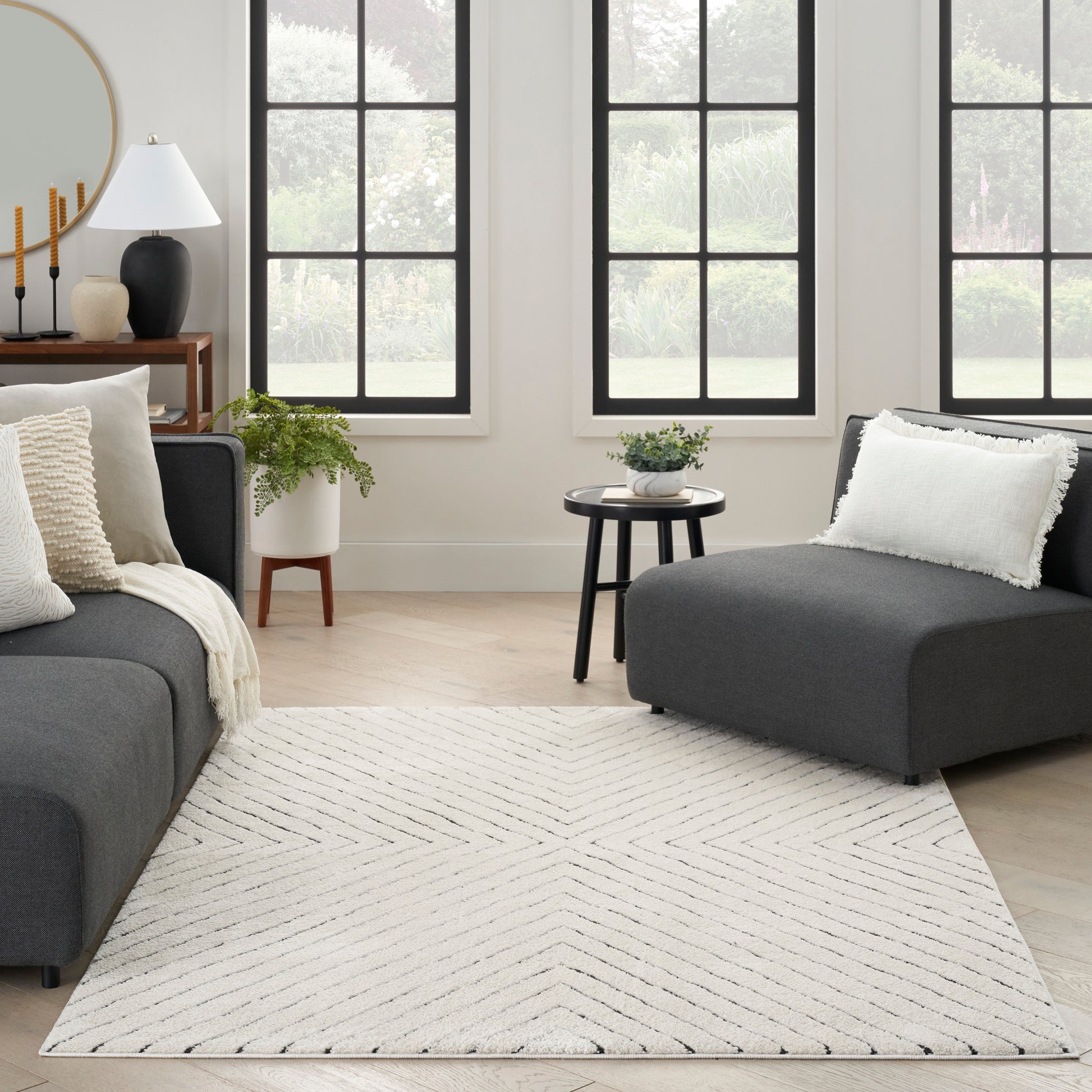 Cream chevron-pattern area rug anchors a modern gray sectional in a bright, plant-filled living room.