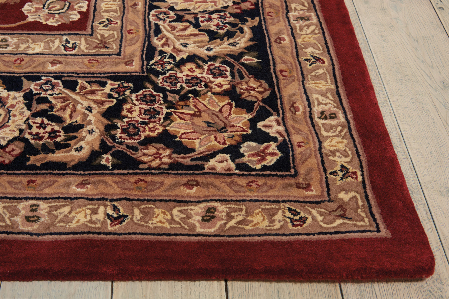 Traditional oriental rug with black central field & gold floral border, red outer edge on light wood floor.