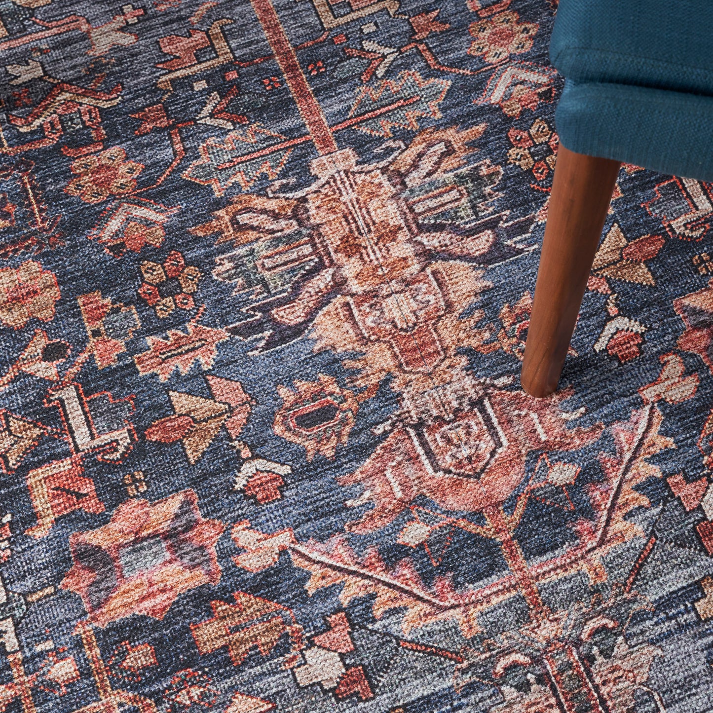 Blue Persian-inspired rug with red and beige floral geometric motifs; wooden chair leg resting on it.
