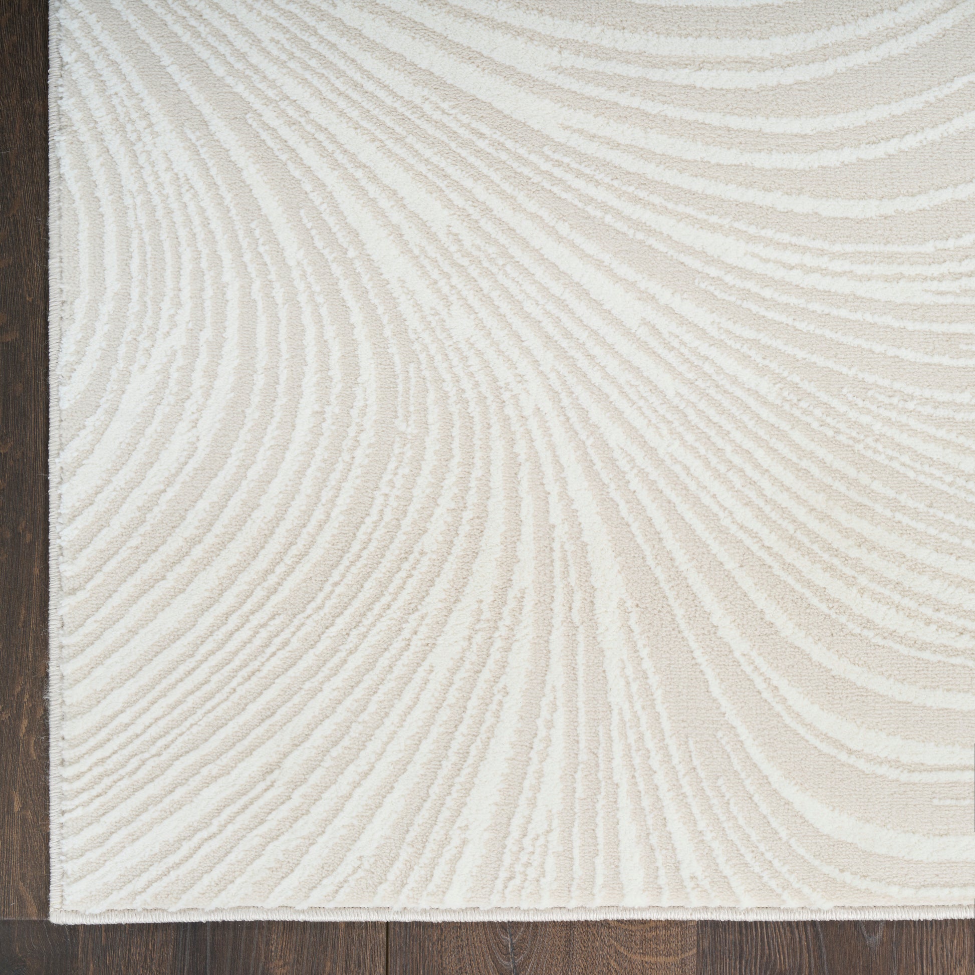 Cream textured area rug with raised beige swirl pattern, dark brown edge binding along left, on wood floor.