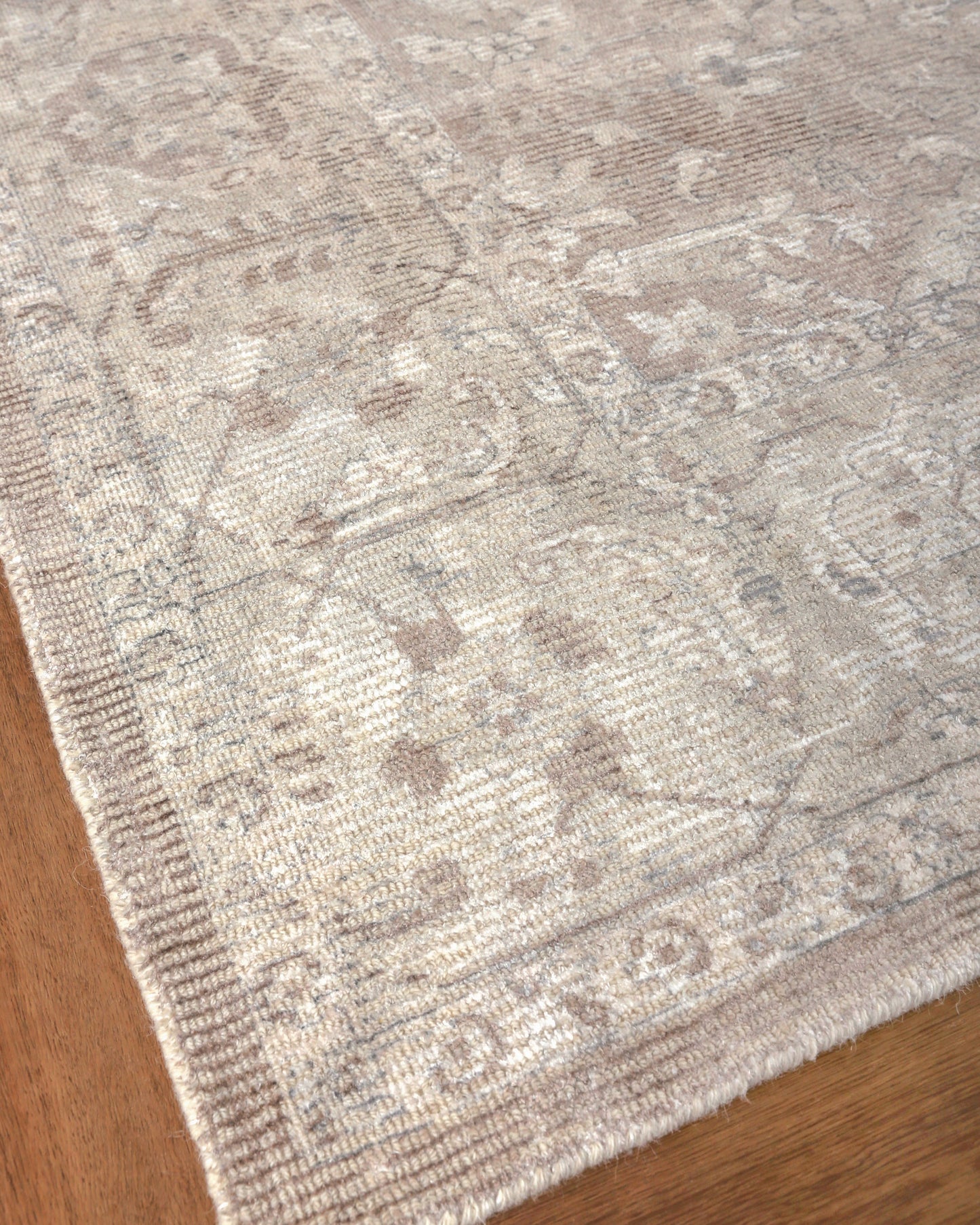 Beige distressed oriental patterned area rug with ornate borders on wooden floor.