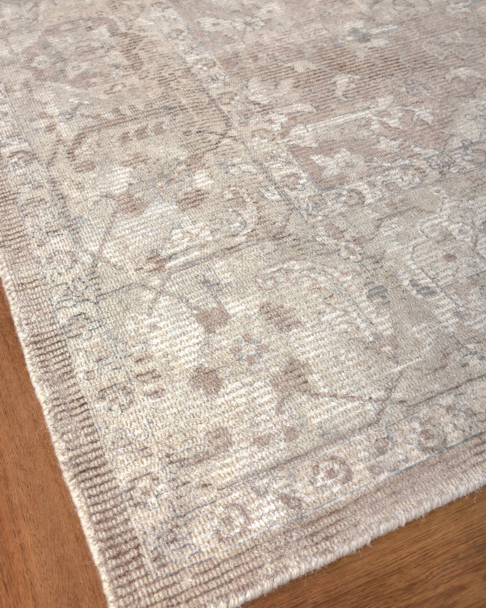 Beige distressed oriental patterned area rug with ornate borders on wooden floor.
