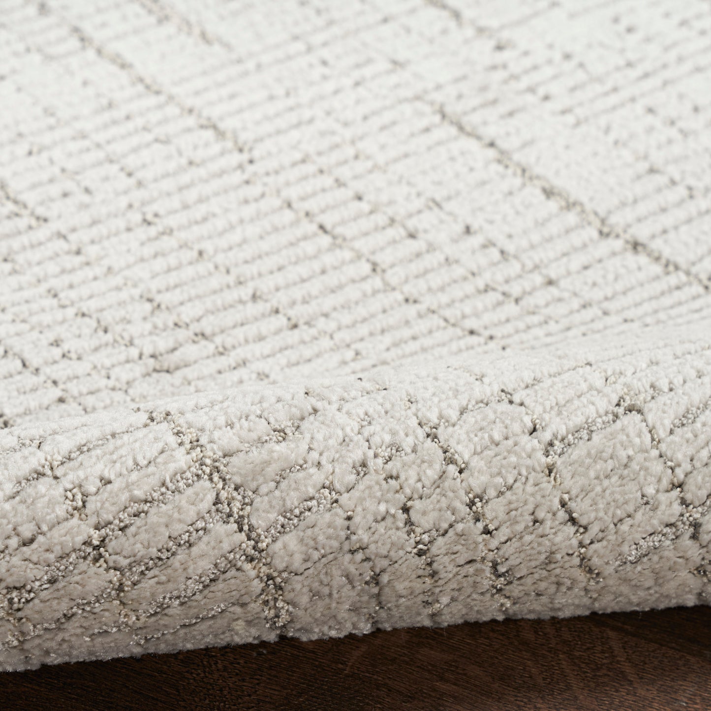 Cream textured rug with diamond pattern, low-pile loop weave, close-up edge on dark wooden floor