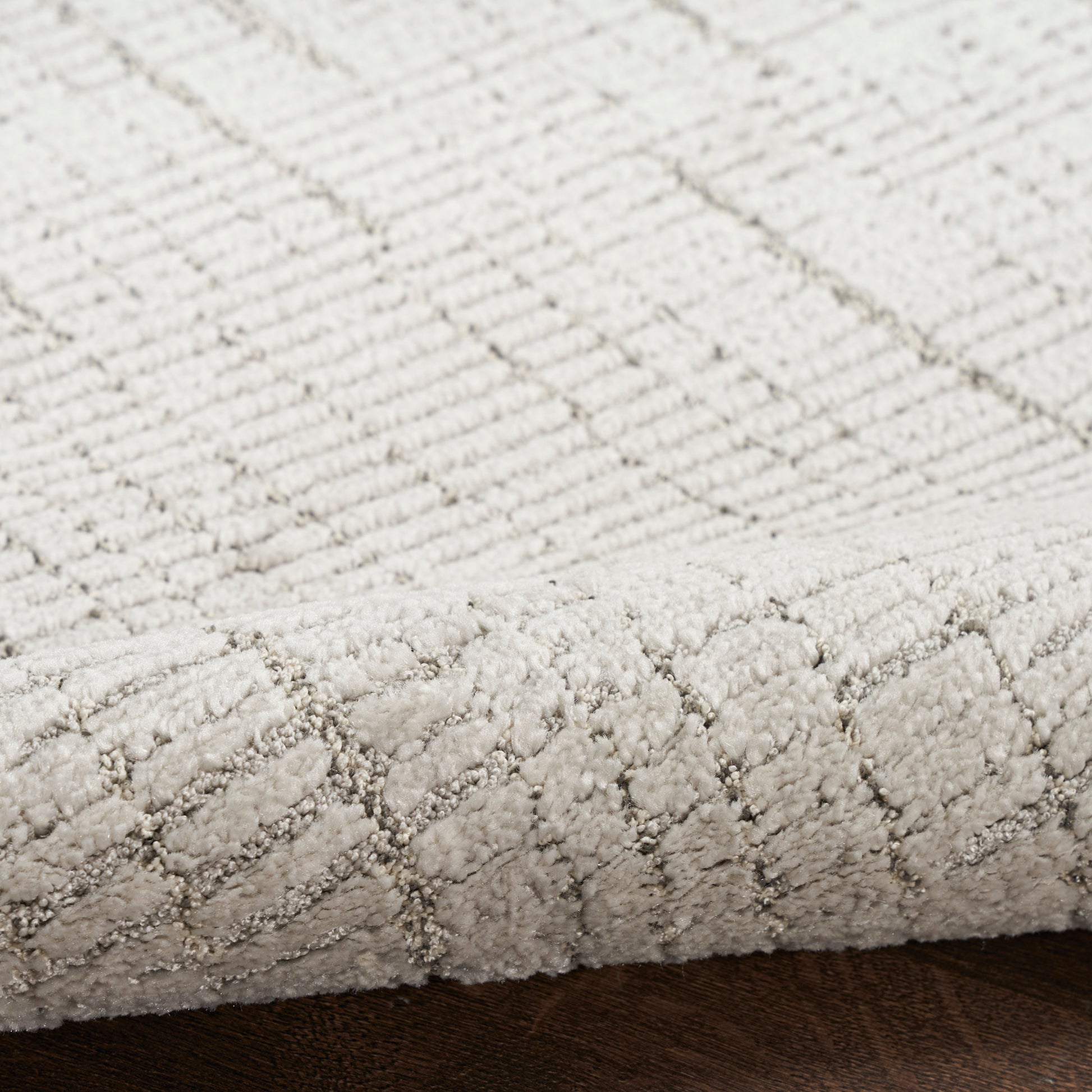 Cream textured rug with diamond pattern, low-pile loop weave, close-up edge on dark wooden floor