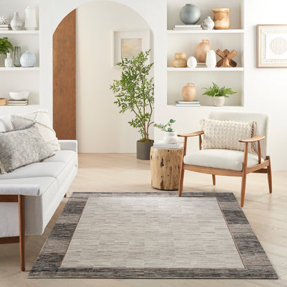 Neutral living room with beige area rug and dark border, light sofa, wooden-armchair, potted tree, and open shelves with ceramics.