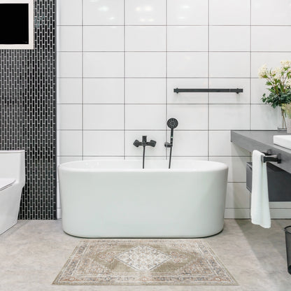 White freestanding tub with matte black fixtures in a modern tiled bathroom, black mosaic wall and beige patterned rug.