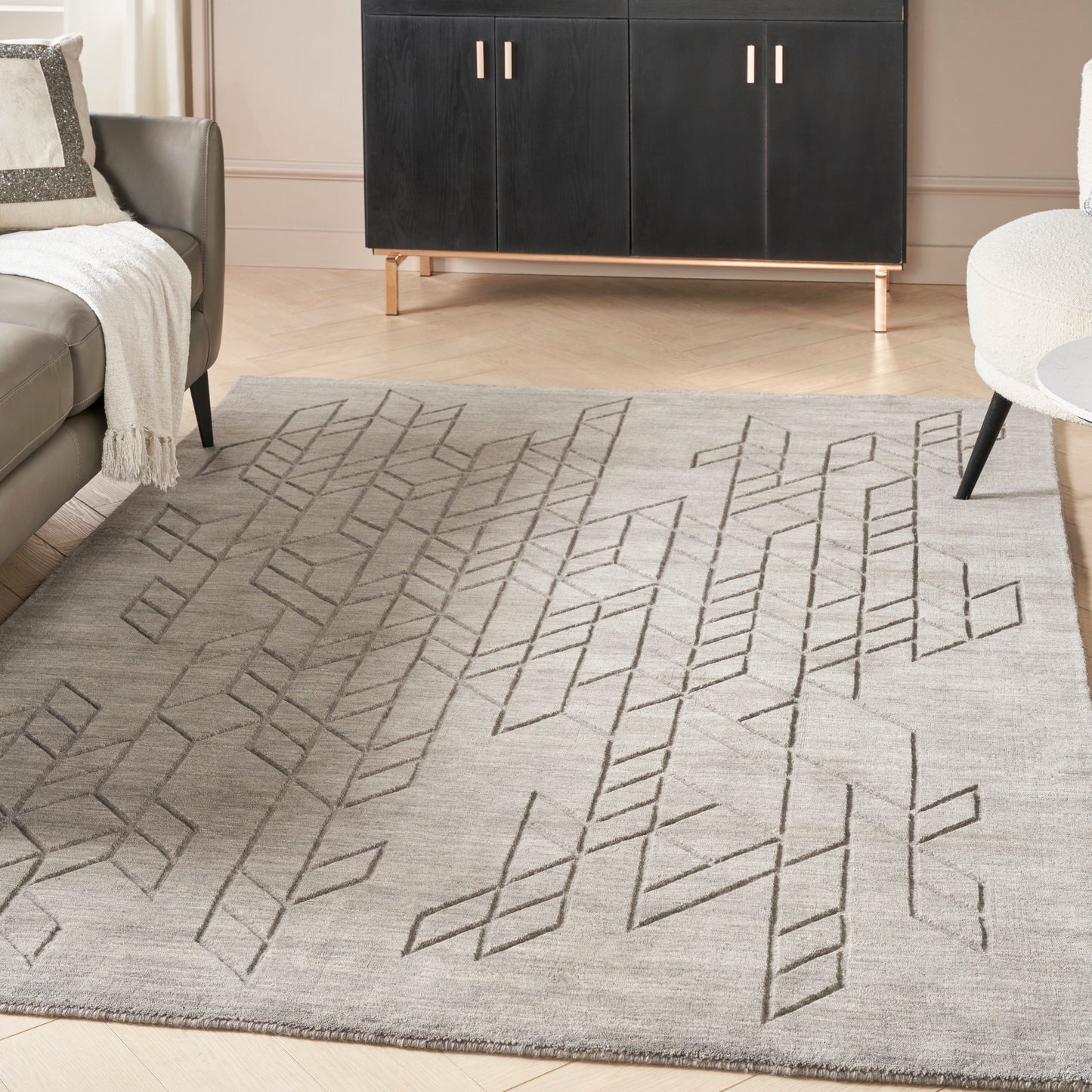 Light gray flatweave rug with dark geometric diamond lattice; modern living room with black cabinet and beige sofa.