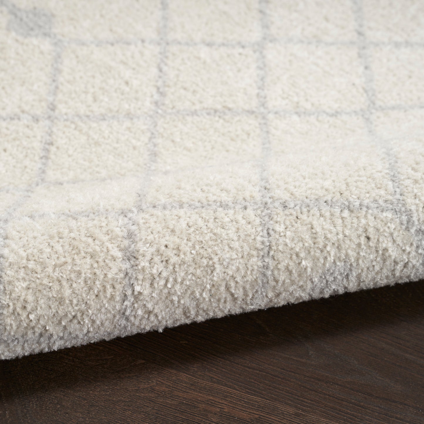 Cream shag runner with a pale gray plaid grid and a folded edge on a dark wood floor.