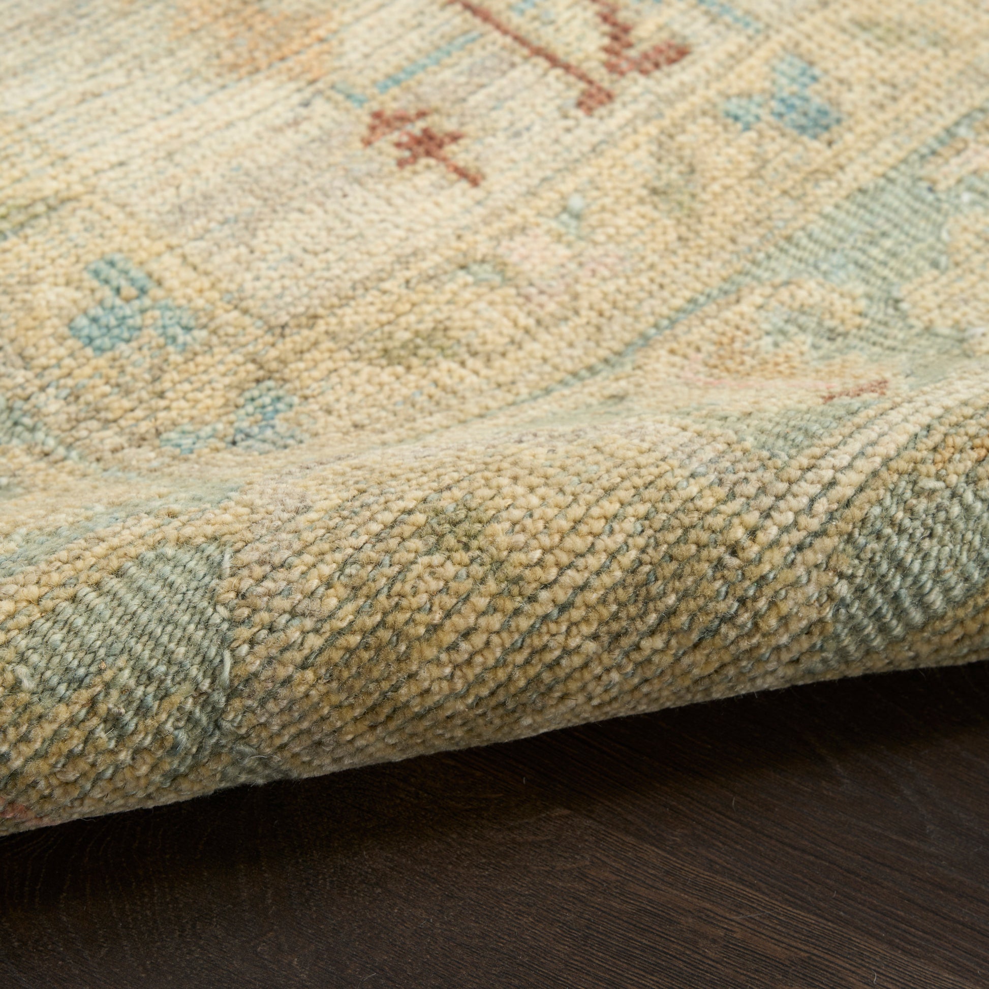 Pastel beige rug with light blue & pink accents, soft woven pile, traditional pattern, folded edge on dark wood floor