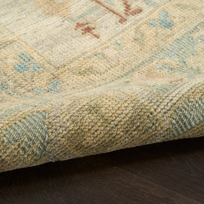 Pastel beige rug with light blue & pink accents, soft woven pile, traditional pattern, folded edge on dark wood floor