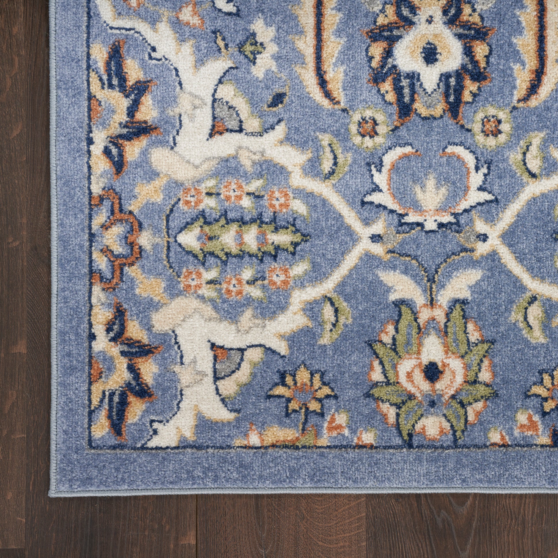 Blue oriental area rug with ivory, orange and green floral motifs and a light blue border on dark wood floor.