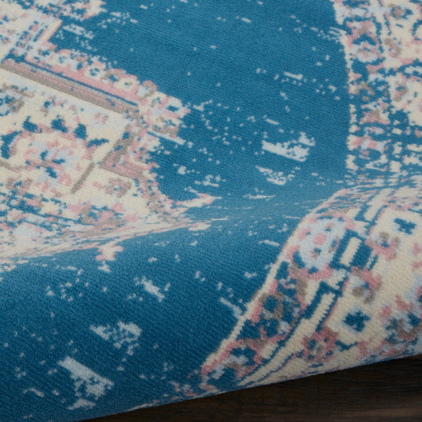 Close-up of a blue oriental rug with ivory-pink floral motifs and a woven texture.