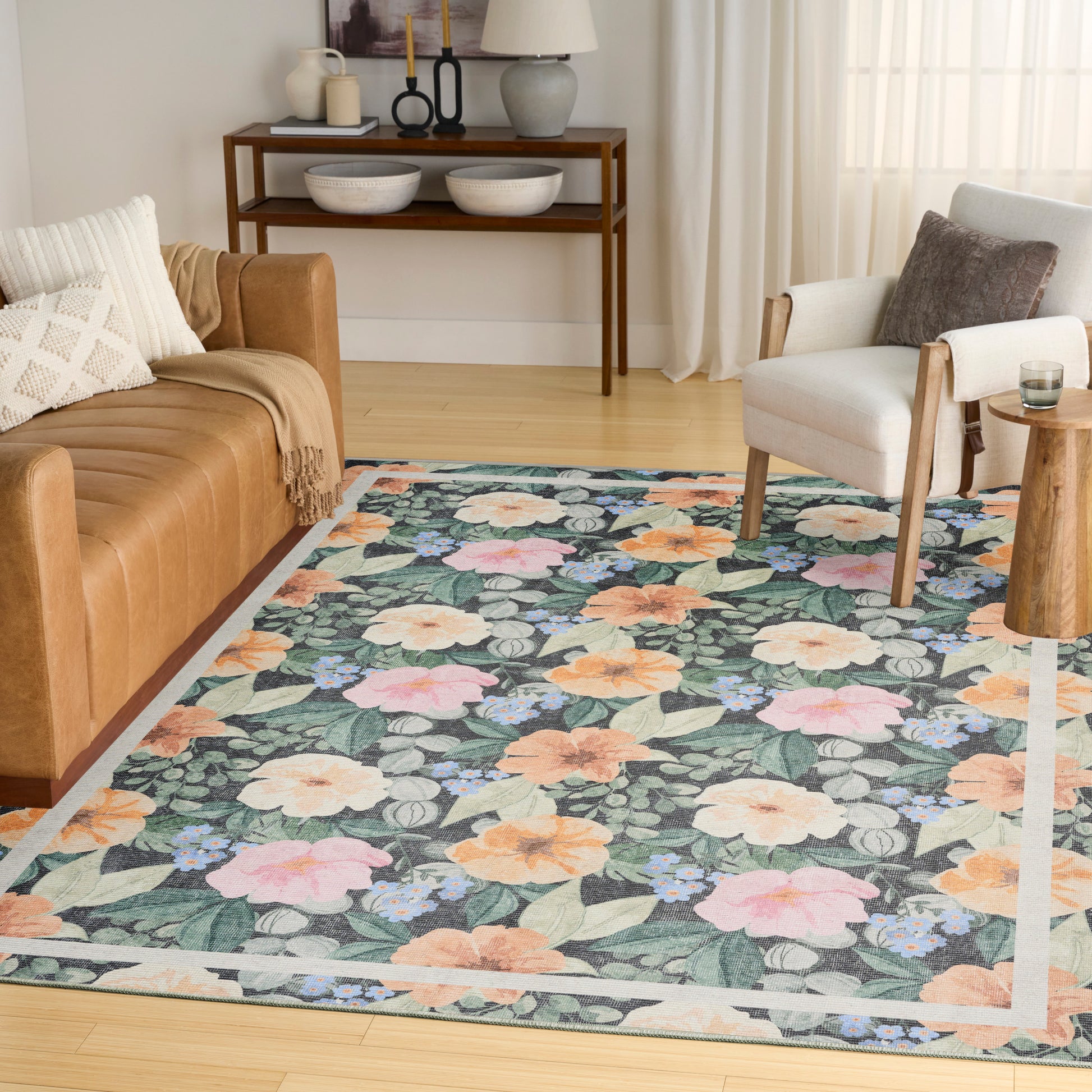 Rectangular floral area rug with pastel peach, pink and yellow flowers on blue-green leaves in a modern living room.