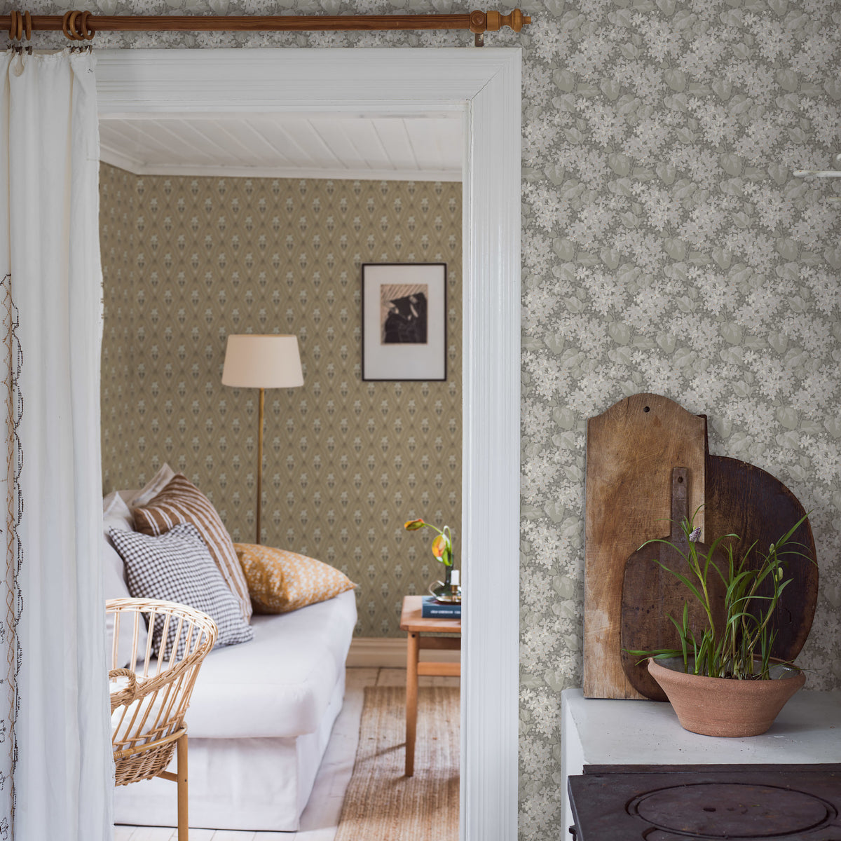 Vintage-style living room seen through a white-trim doorway; grey stone-look wallpaper, wicker chair, white sofa & a plant on wood boards.
