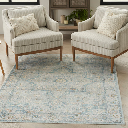 Blue patterned area rug on the floor with two beige striped armchairs and textured throw pillows
