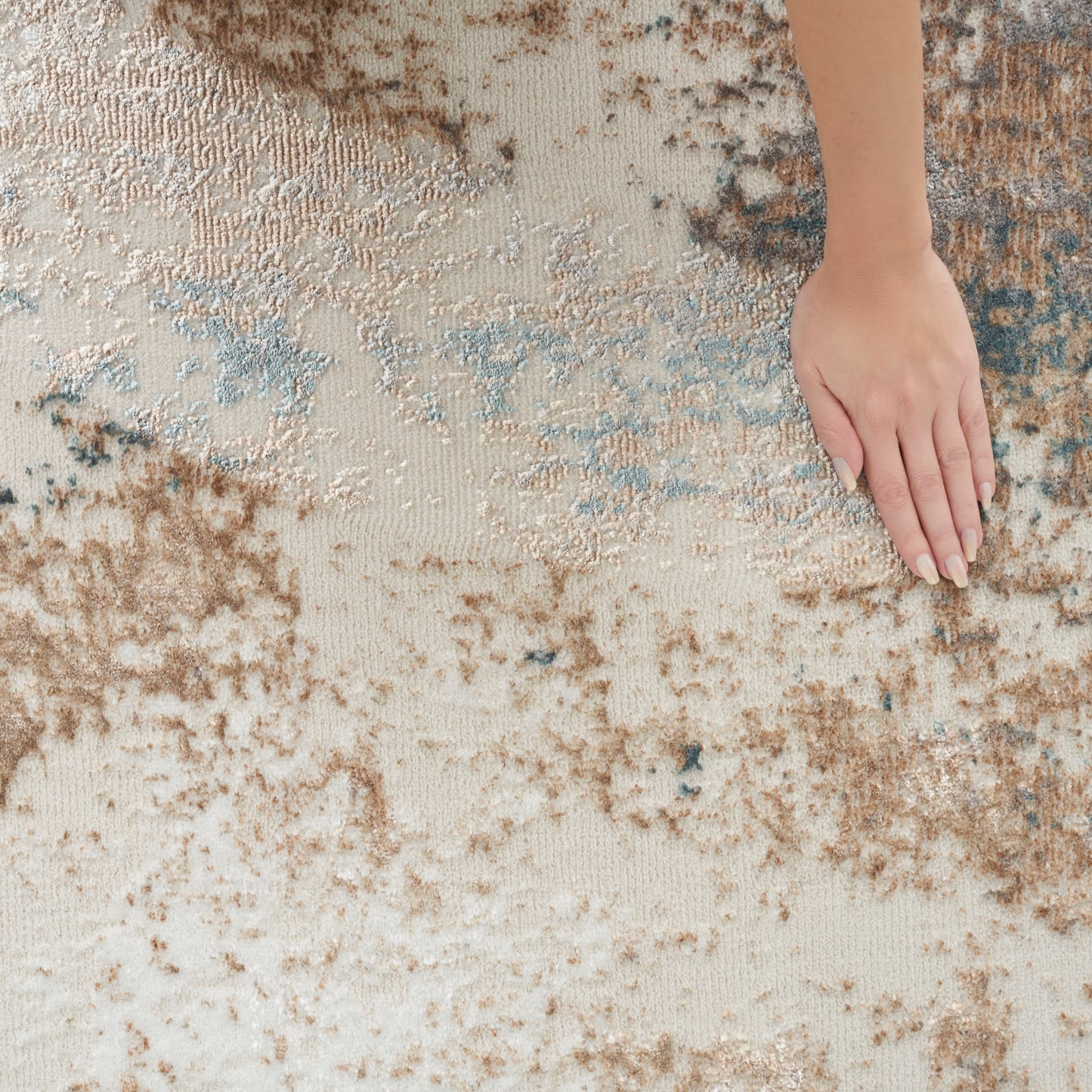 Beige and brown abstract patterned rug with blue accents; soft textured pile, hand resting on surface.