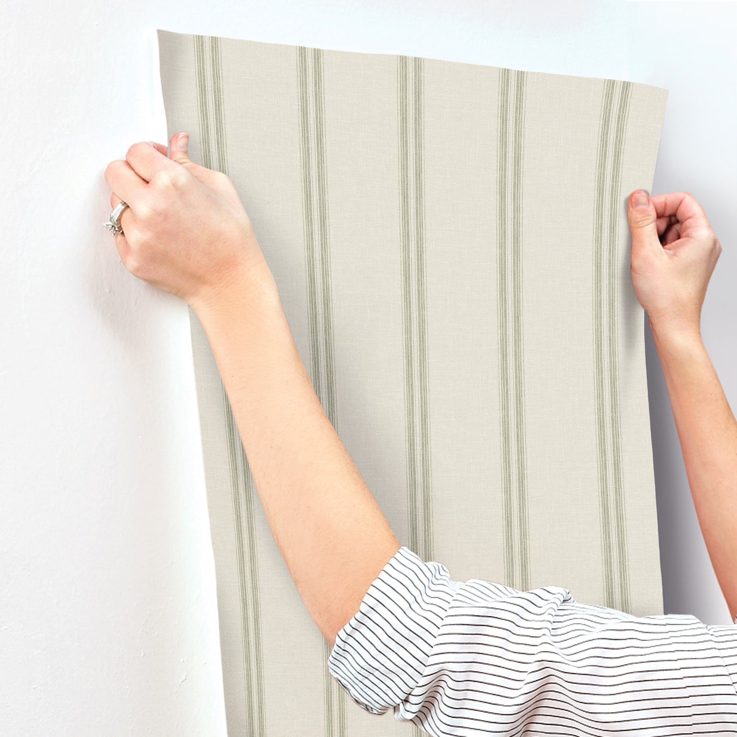 Two hands hold a green striped wallpaper panel with vertical stripes, ready for wall placement.