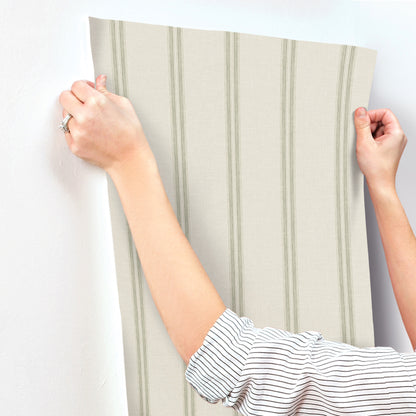 Two hands hold a green striped wallpaper panel with vertical stripes, ready for wall placement.