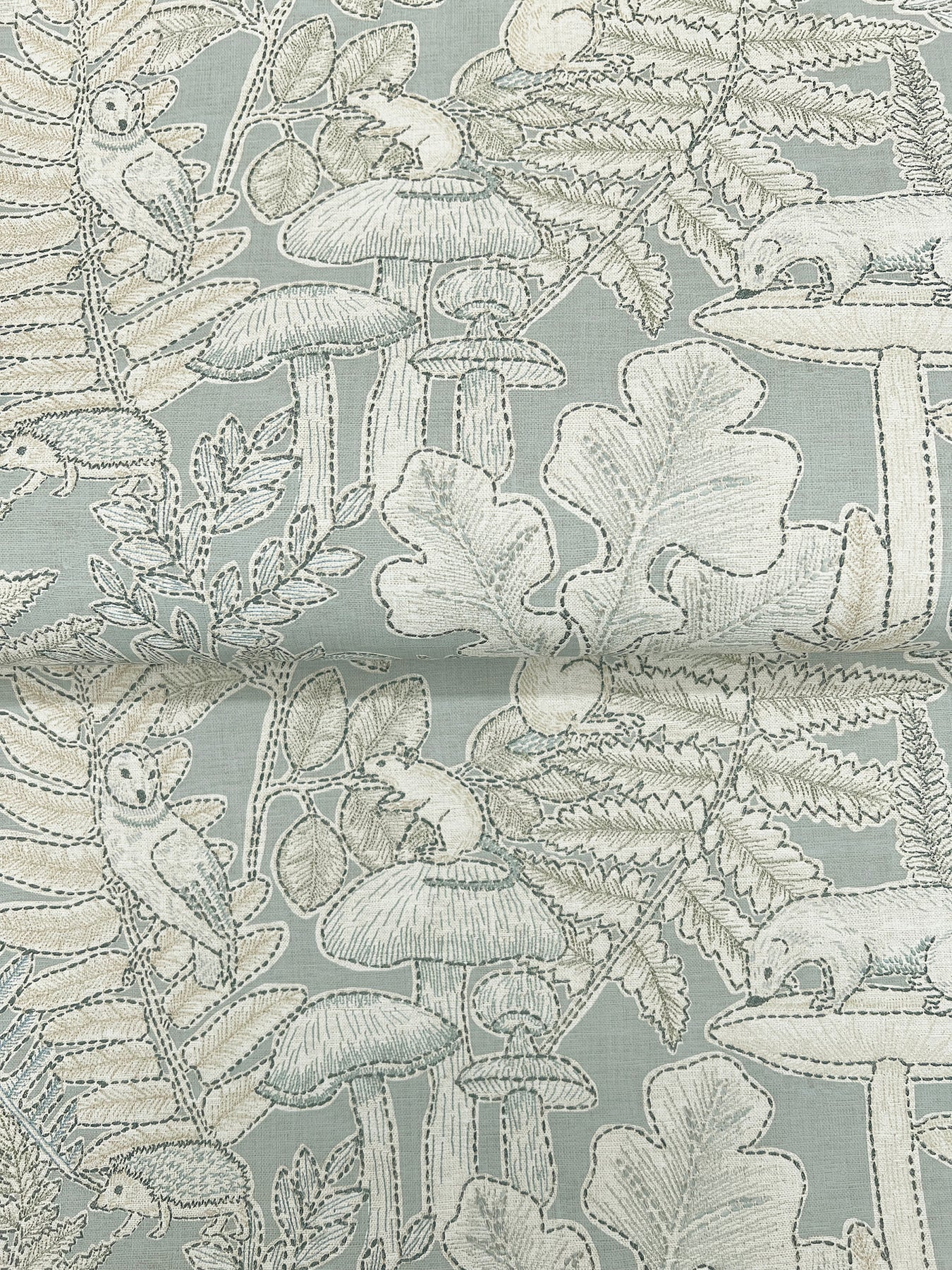 Pale blue-gray fabric with white line-drawn woodland mushrooms, ferns and leaves pattern.