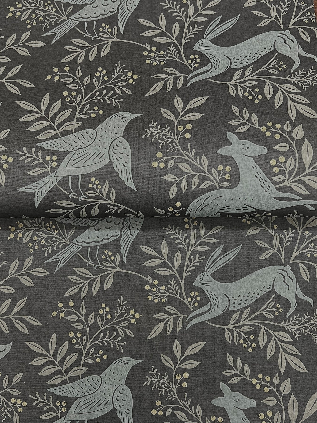 Dark gray fabric with pale blue-gray botanical motif: birds, leaves, berries, and a hare, nature-inspired textile.
