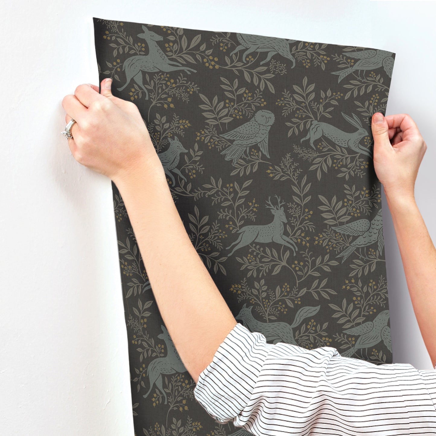 Hands hold a sheet of dark charcoal wallpaper featuring grey birds and leafy foliage pattern
