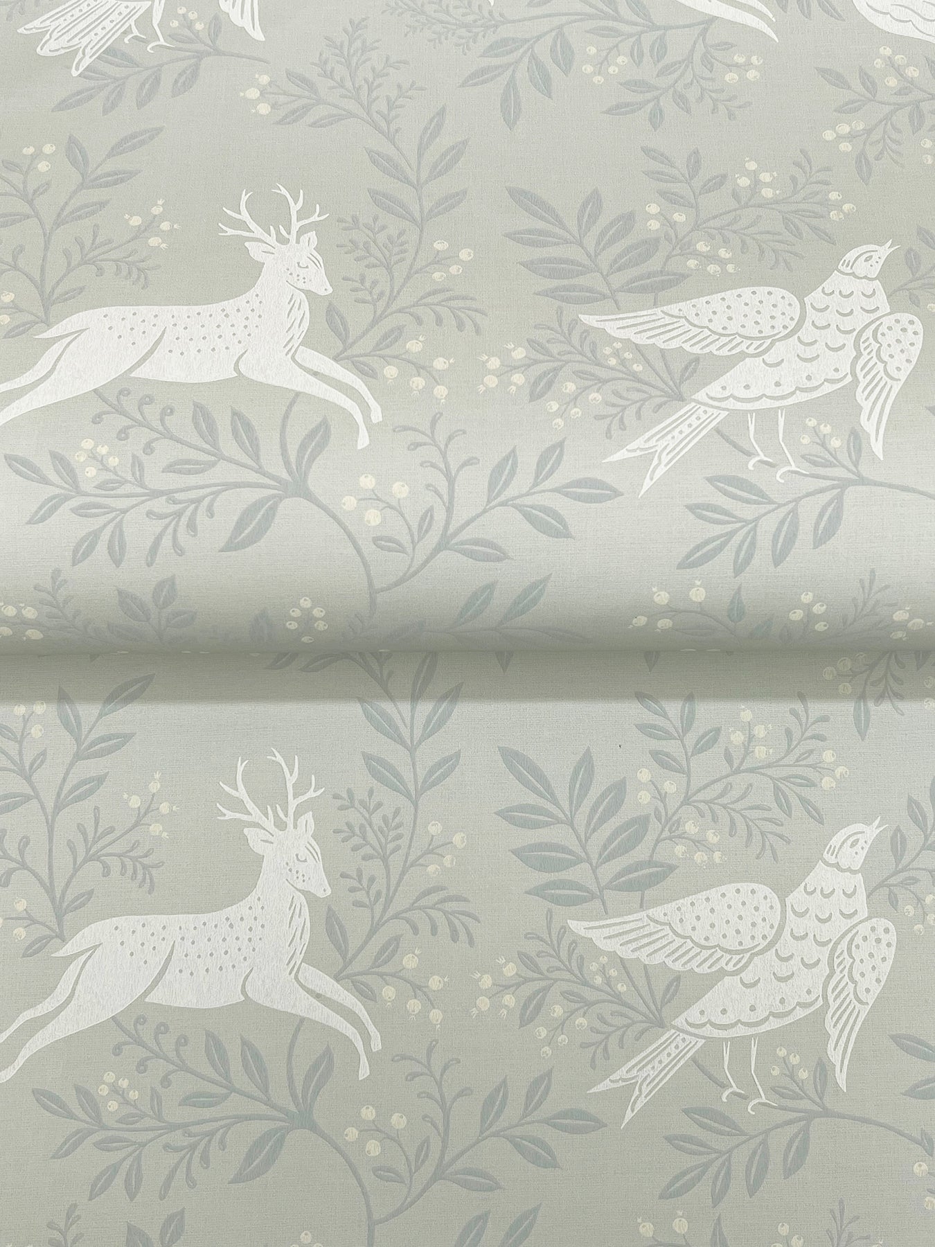 Soft sage green wallpaper with a white woodland motif of leaping deer and birds among leafy branches.
