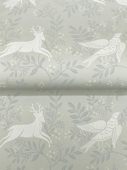 Soft sage green wallpaper with a white woodland motif of leaping deer and birds among leafy branches.