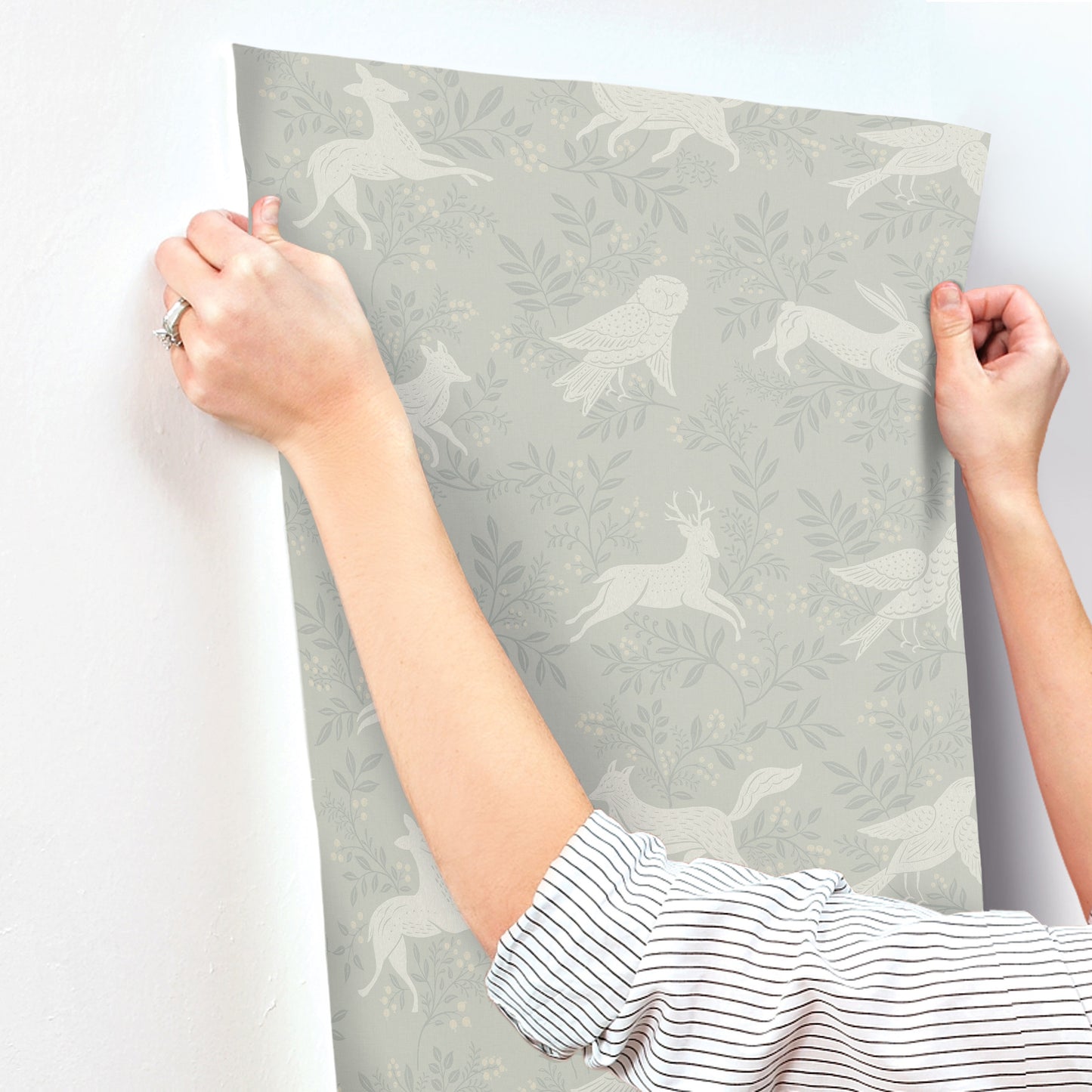Gray wallpaper panel with white birds and foliage pattern; edges held by hands, striped sleeves visible.