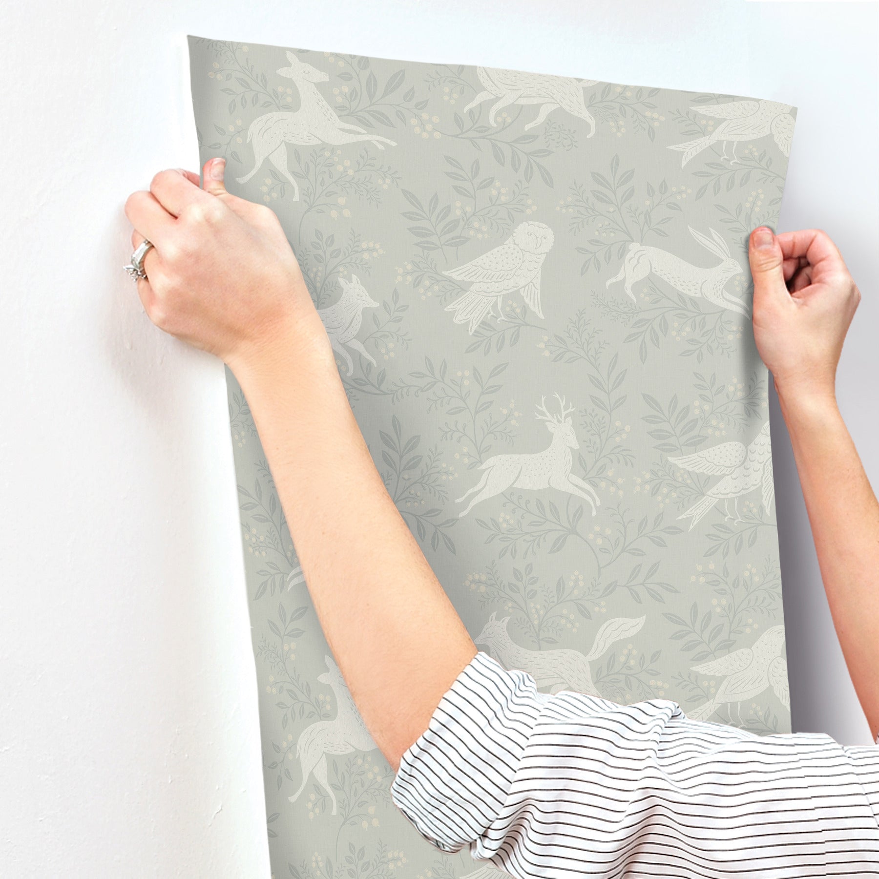 Gray wallpaper panel with white birds and foliage pattern; edges held by hands, striped sleeves visible.