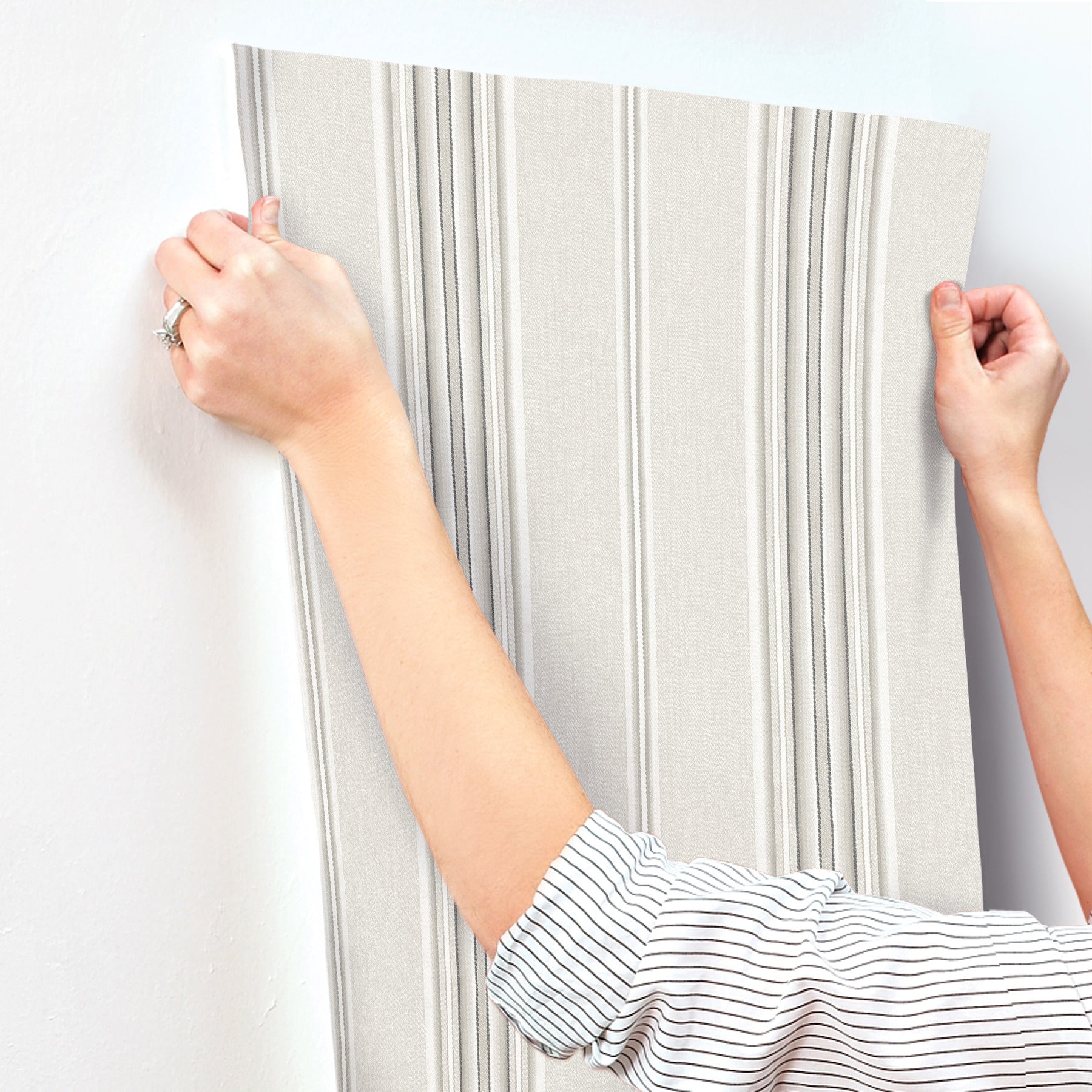Beige wallpaper sample with vertical gray stripes; embossed texture, held by hands for interior wall decor.