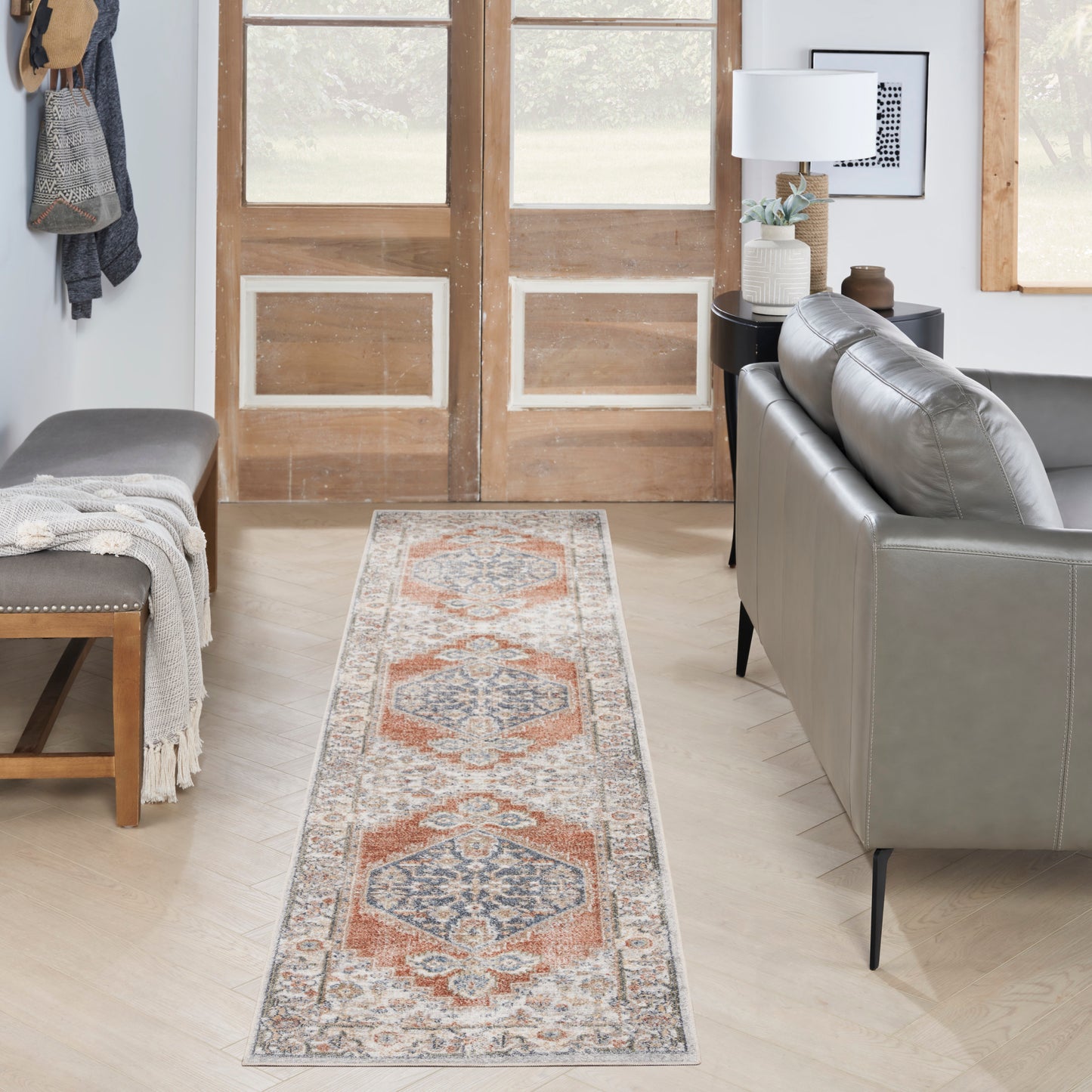 Long runner rug with orange, blue and cream geometric pattern on light wood floor beside a grey sofa in a modern living room.