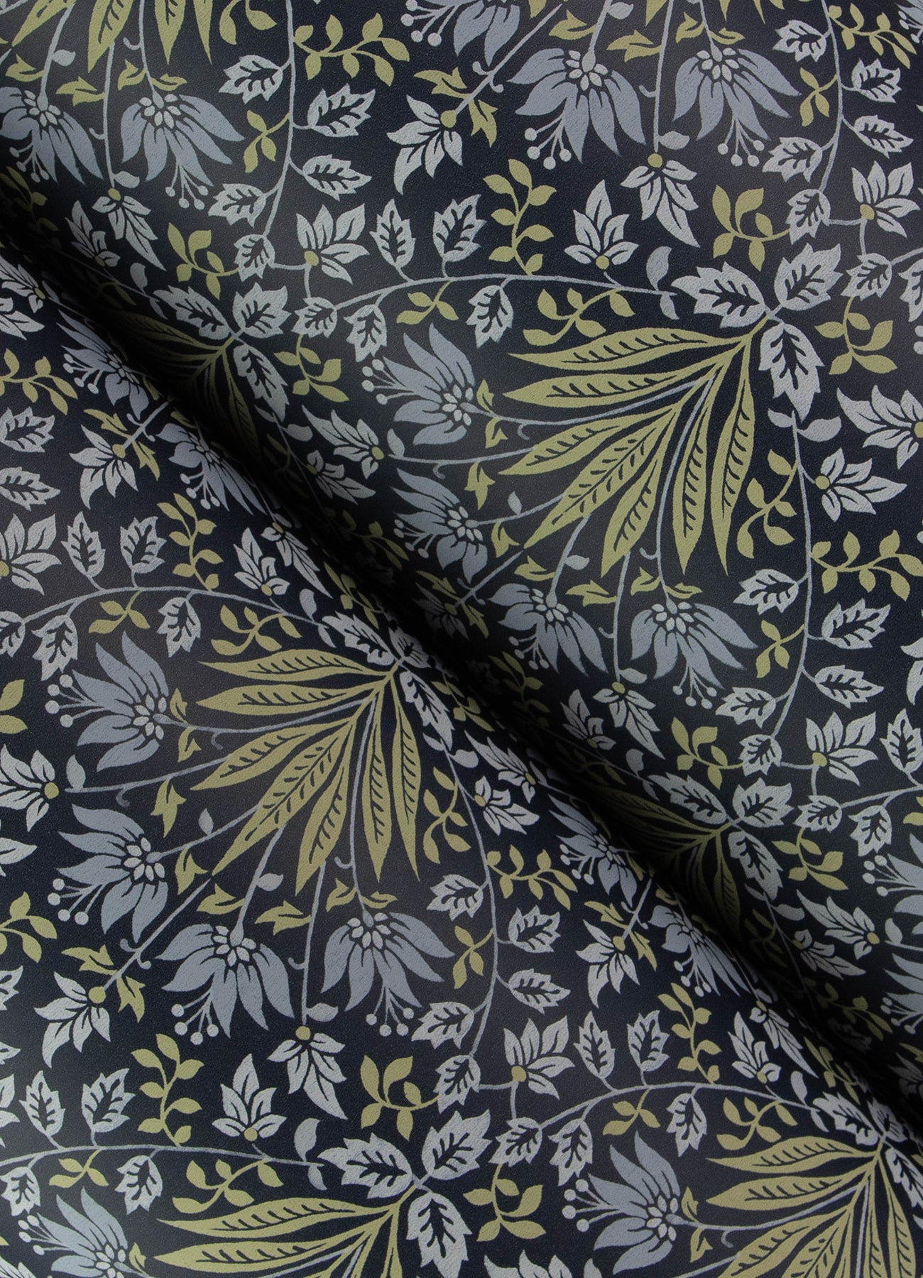 Close-up of navy fabric with olive-green and light-blue botanical leaves; folded, textile print for clothes or decor.