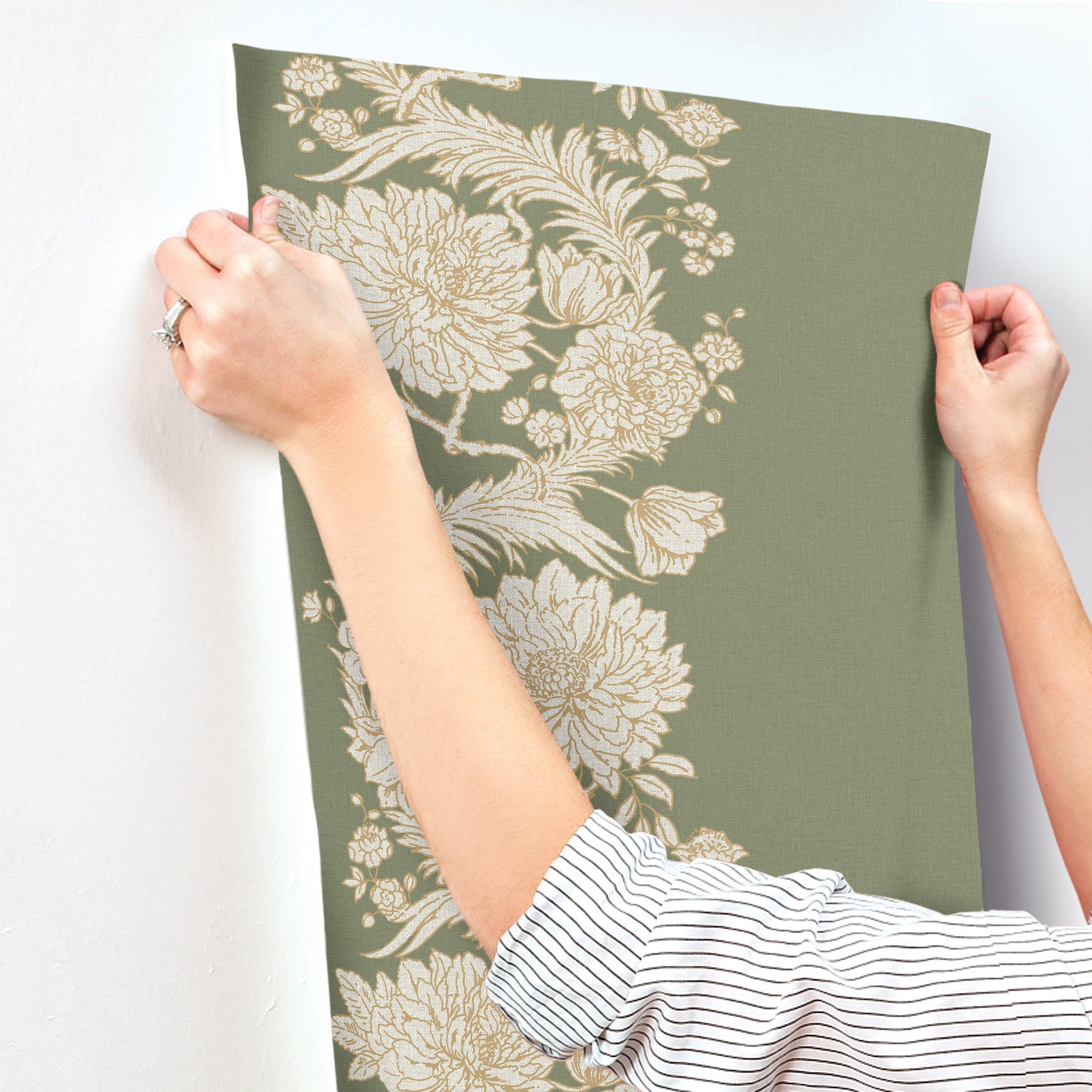 Person holds olive-green wallpaper panel with large cream floral pattern, vintage botanical style