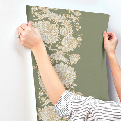 Person holds olive-green wallpaper panel with large cream floral pattern, vintage botanical style