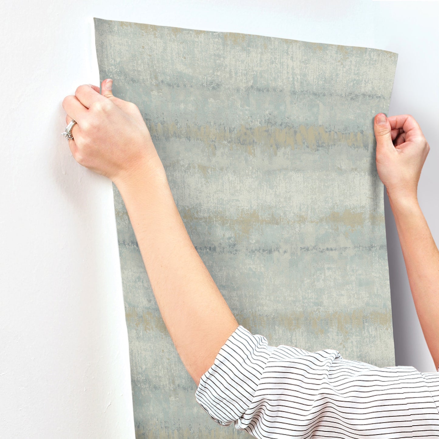 Light blue textured stripe wallpaper swatch being held by hands, showing a modern wallcovering.