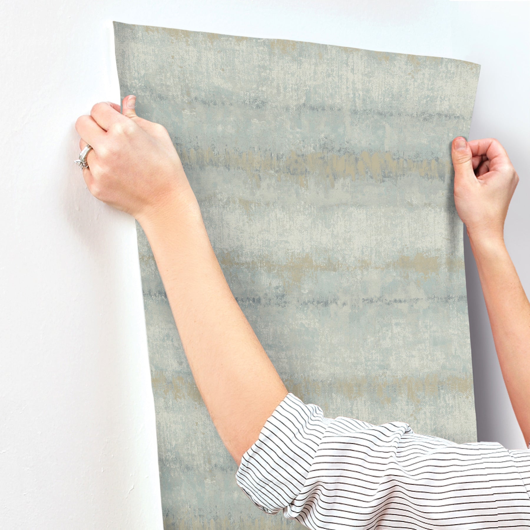 Light blue textured stripe wallpaper swatch being held by hands, showing a modern wallcovering.