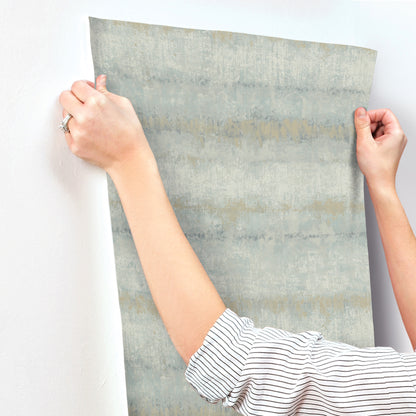 Light blue textured stripe wallpaper swatch being held by hands, showing a modern wallcovering.