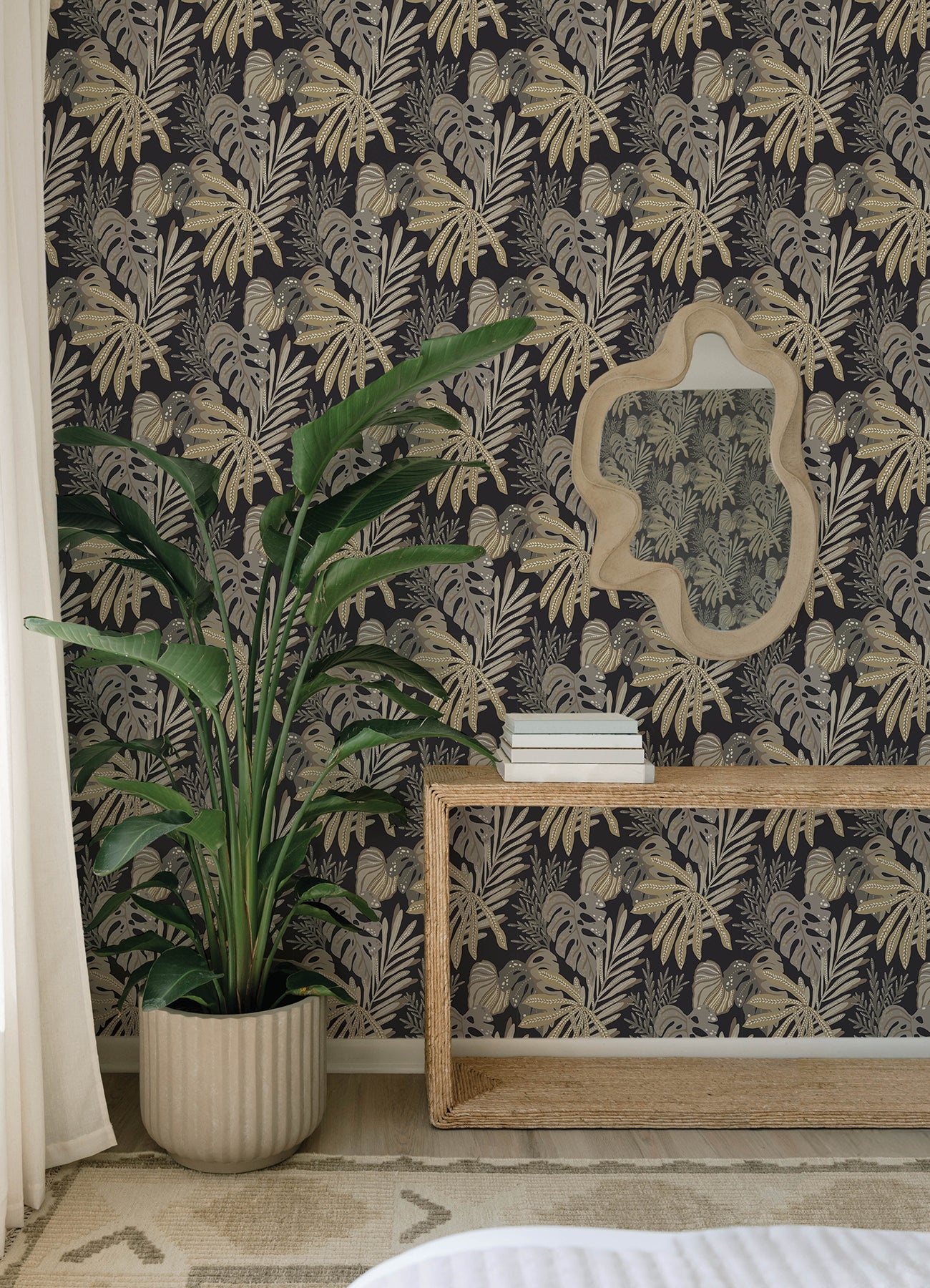 Black botanical wallpaper with beige palm leaves, large green plant in ribbed beige pot, beige mirror above rattan console.