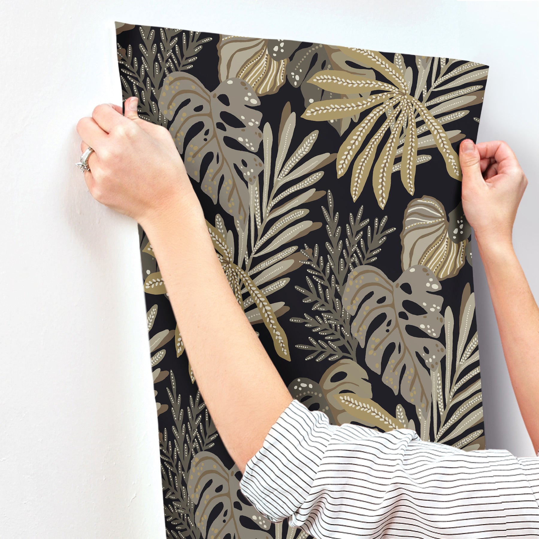 Gold and taupe tropical leaf print on black background, poster being hung as wall decor.